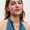 A woman wearing a denim halter top and a silver necklace with a heart pendant. Náhled obrázku produktu