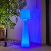 A tall, cone-shaped lamp with a pleated shade, illuminated with blue light, stands on a patio next to a tree. Produktbild-Vorschau