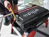 A person is using a handsaw to cut a piece of metal or plastic, with a large black tool case with red accents in the foreground. Produktbild-Vorschau
