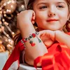 A young girl wearing a Christmas-themed bracelet, with festive lights in the background. Náhľad obrázku produktu