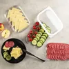 A top-down view of food items arranged on a gray surface, including cheese slices, cherry tomatoes, cucumber slices, salami, and apples, alongside clear plastic food storage containers. Produktbild-Vorschau