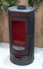 A black freestanding wood-burning stove with a red interior is shown against a light-colored surface and a wooden background with greenery at the top. Náhľad obrázku produktu
