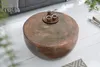 A round copper coffee table with a hammered finish is shown in a living room setting, with a sofa and throw blanket visible in the background. Produktbild-Vorschau