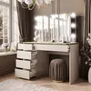A modern vanity table with a lighted mirror, drawers, and a stool, set in a well-lit room with large windows and curtains. Produktbild-Vorschau