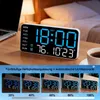A digital clock displaying time, temperature, and day of the week, shown on a table next to a laptop and a cup of coffee. Below the main clock image, there are smaller images demonstrating different brightness levels. Produktbild-Vorschau