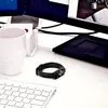 A black fitness tracker is placed on a white desk next to a white keyboard and a white mug. Voir les images du produit