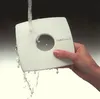 A hand holding a white square object with a circular cutout under running water. Podgląd zdjęcia produktu