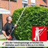 A man is using a telescopic hedge trimmer to trim a large green hedge in front of a brick house. Produktbild-Vorschau