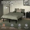 A metal bed frame with bedding and pillows, set in a bedroom with a floor lamp and nightstand. Podgląd zdjęcia produktu