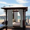 A cabana with curtains on a beach with umbrellas and boats in the background. Voir les images du produit