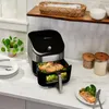 An air fryer on a kitchen counter with food inside and on a plate. Produktbild-Vorschau