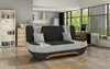 A modern living room with a sofa, kitchen area, and desk by a large window.