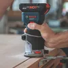 A person is using a Bosch cordless router on a wooden surface. Voir les images du produit