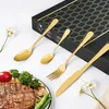 A set of gold-colored cutlery is displayed on a white surface, with a steak and vegetables in the foreground and a gift box in the background. Produktbild-Vorschau