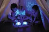 Three children are sitting inside a tent, looking at glowing toys. Voir les images du produit