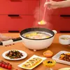 Weißer elektrischer Topf mit schwarzer Innenfläche, kochendes Essen, von einer Hand gehalten, umgeben von verschiedenen Gerichten auf einem braunen Tisch Produktbild-Vorschau
