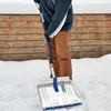 A person is using a snow shovel to clear snow in front of a wooden fence. Produktbild-Vorschau