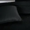 A close-up view of a black quilted blanket or bedspread with a geometric triangle pattern. Produktbild-Vorschau