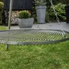A close-up of a round metal grill grate suspended by chains over a grassy lawn, with large planters and a woodpile in the background. Podgląd zdjęcia produktu