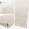 A collage of close-up shots of a beige and cream-colored rug with a subtle bear motif. One shot shows the rolled-up edge of the rug, revealing the backing. Produktbild-Vorschau