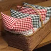 A wicker basket filled with checkered pillows on a wooden surface. Produktbild-Vorschau