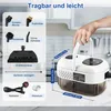 A hand holding a portable steam cleaner with various accessories laid out next to it, in a kitchen-like setting. Produktbild-Vorschau