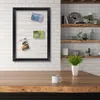 A black framed collage board with three photos attached, hanging on a white brick wall above a wooden table with a mug and a potted plant. Produktbild-Vorschau