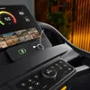 Close-up view of a treadmill's console, showing a smartphone charging and various workout videos displayed on the screen. Produktbild-Vorschau
