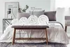 A bedroom scene with a bed and rolled-up duvets displayed on a bench in front of it. Produktbild-Vorschau