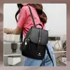 A woman wearing a pink shirt and blue jeans is posing with a black leather backpack. Voir les images du produit