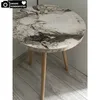 A round side table with a marble-like top and wooden legs, placed on a wooden floor. Produktbild-Vorschau