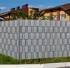A close-up view of a gray privacy screen fence installed in a garden setting, with houses visible in the background. Produktbild-Vorschau