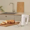 A white hand mixer with bread on a cutting board in a kitchen setting. Produktbild-Vorschau