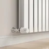 A close-up shot of a white radiator thermostat valve attached to a white radiator and a light-colored wall. Náhled obrázku produktu