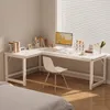 A white L-shaped desk with a computer and office supplies is set up in a room with natural light coming from a window with blinds. Produktbild-Vorschau