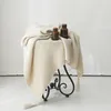 A knitted blanket draped over a small, ornate metal stool, with two decorative glass bottles on top. Produktbild-Vorschau