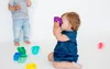 Two babies are playing with colorful cups on a white background. Produktbild-Vorschau