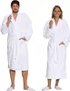 A man and a woman are standing side-by-side, both wearing white bathrobes and slippers. Produktbild-Vorschau