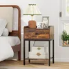A bedside table with a lamp, picture frames, and storage boxes next to a bed. Podgląd zdjęcia produktu