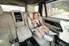 A child is sitting in a car seat in the back of a luxury car. Voir les images du produit