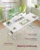 A white standing desk with a monitor, laptop, and accessories, set up in a bright, modern room with a rug and plants. Produktbild-Vorschau