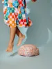 A person in a colorful checkered dress is jumping over a large, round object covered in colorful sprinkles. Produktbild-Vorschau