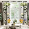 Two S-shaped flower stands with various flowers are displayed in a living room setting with a large window in the background. Anteprima dell’immagine prodotto