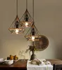 Three geometric pendant lights hang above a wooden dining table set with fruit, bottles of water, and folded napkins. Náhľad obrázku produktu