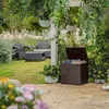 A garden storage box is shown in a lush garden setting, with outdoor furniture and hanging plants. Podgląd zdjęcia produktu