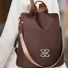 Brauner diebstahlsicherer Rucksack mit hellbraunen Trägern und silbernem ineinandergreifendem Logo, auf der Schulter einer Person getragen Anteprima dell’immagine prodotto