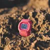 A pink G-Shock watch rests on a rocky, sandy surface. Produktbild-Vorschau