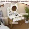 A white vanity table with a cat-ear shaped mirror and lights, set up in a bedroom next to a bed and a plant. Podgląd zdjęcia produktu