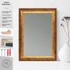 A decorative antique-style mirror with a bronze-colored frame, displayed on a white surface next to a vase with dried flowers. Produktbild-Vorschau