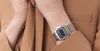 A close-up shot of a person's wrist wearing a silver digital watch with a mesh band, against a brown fabric background. Voir les images du produit